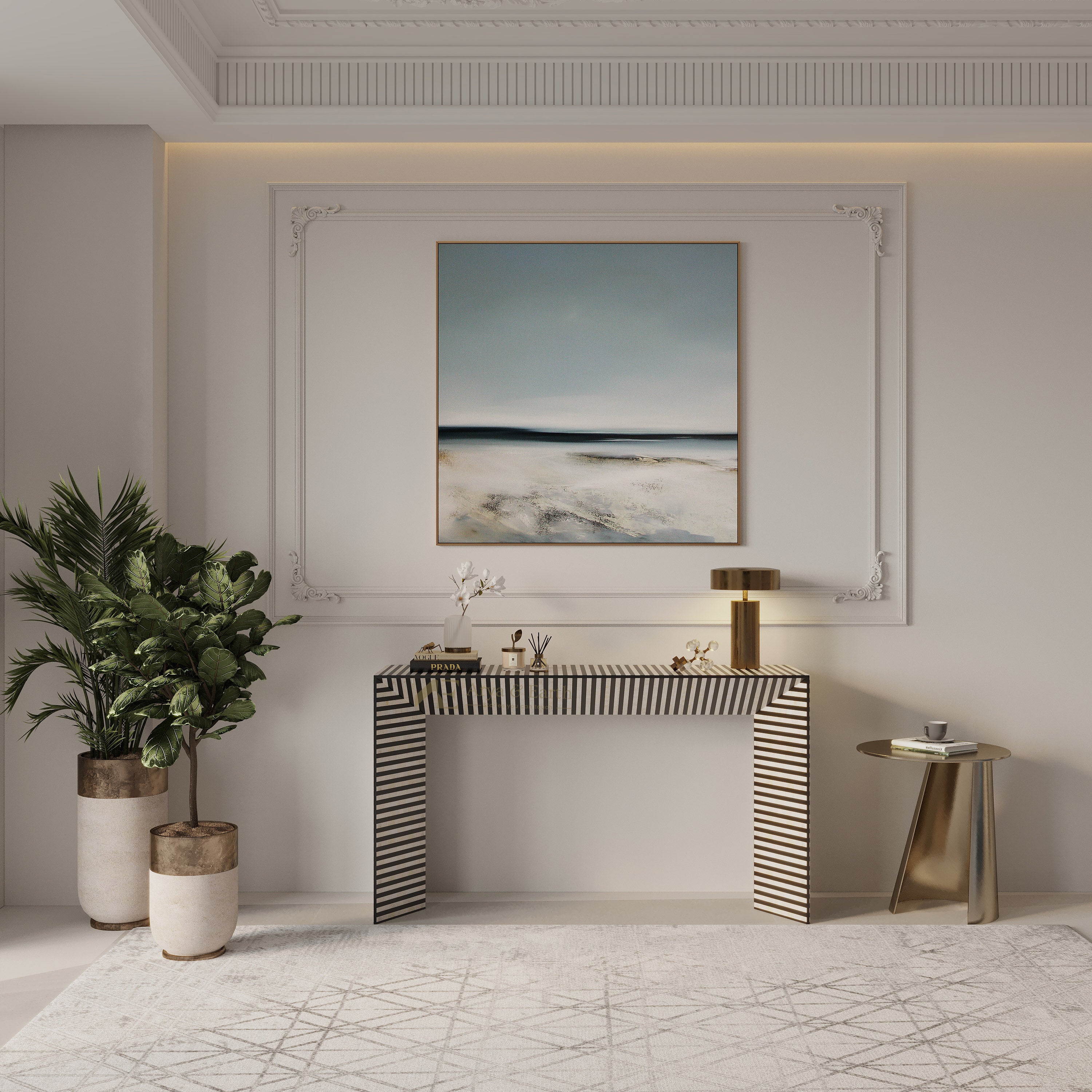 A framed abstract landscape painting with blue, gray, and beige tones hangs on a white wall above a striped console table in a modern, elegant interior setting.