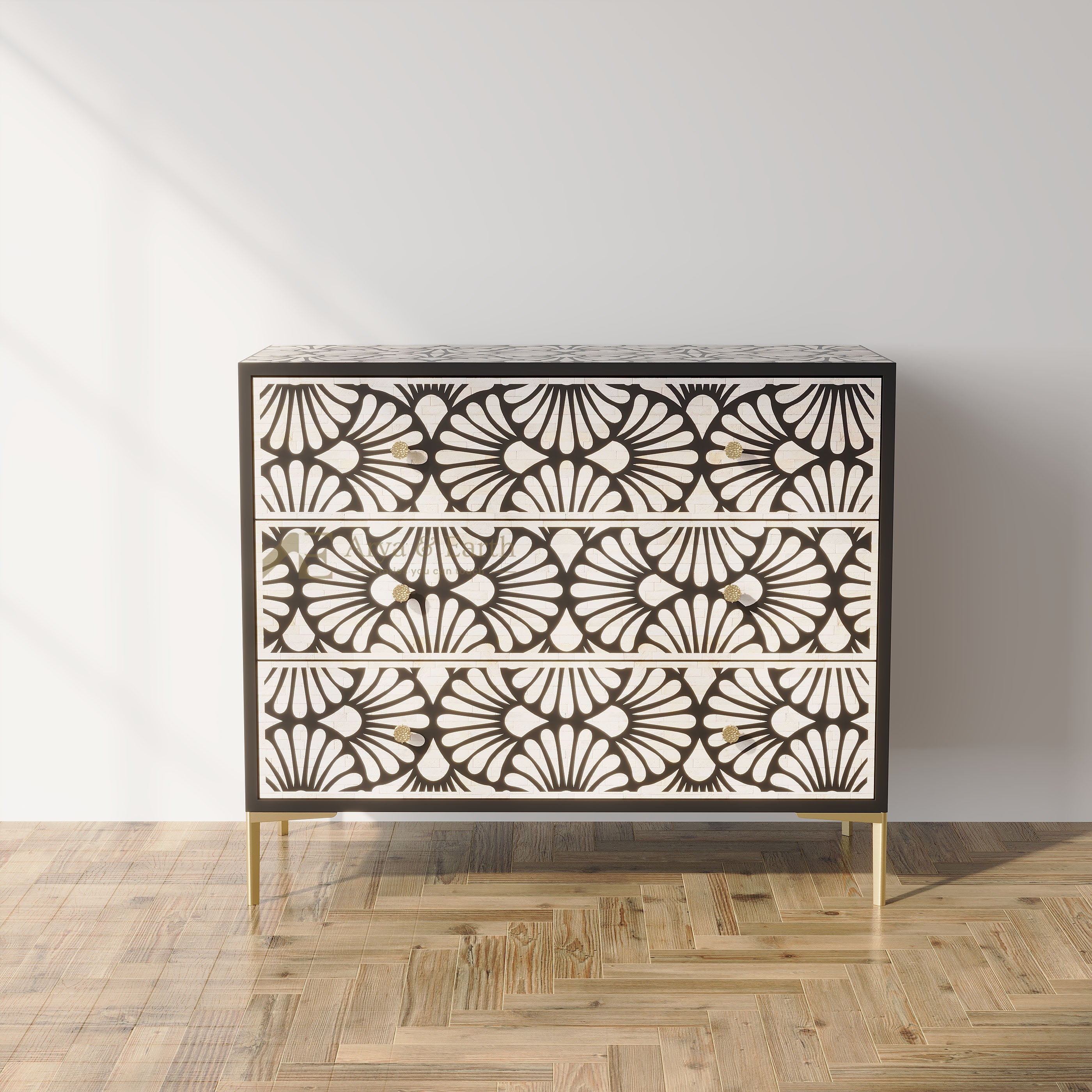 A three-drawer chest with an intricate black and white geometric floral pattern and gold-tone legs, set against a light gray wall and a herringbone wood floor.