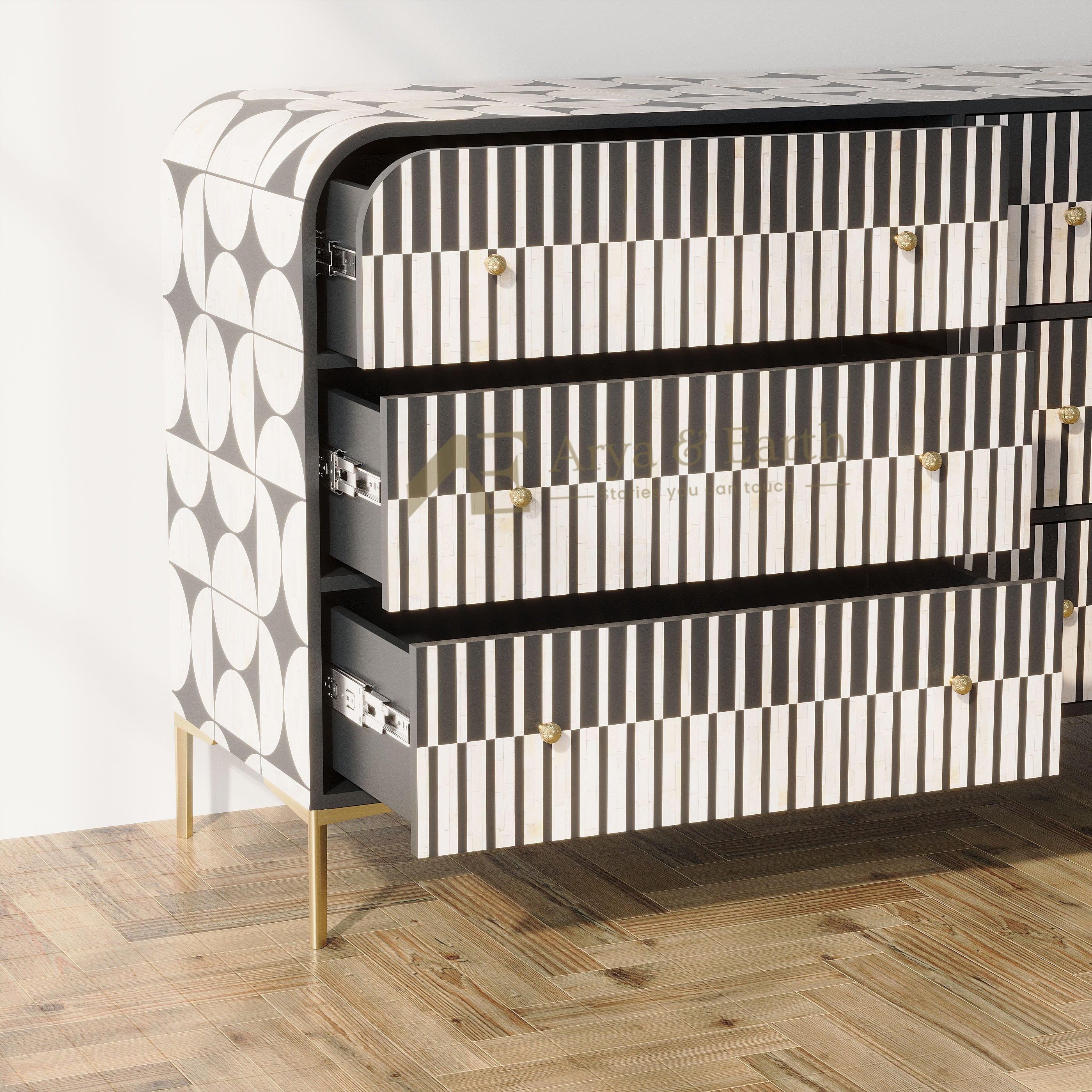 A modern three-drawer chest of drawers with a black and white striped and geometric pattern, featuring gold-tone handles and legs, set on a light wood herringbone floor against a white wall.