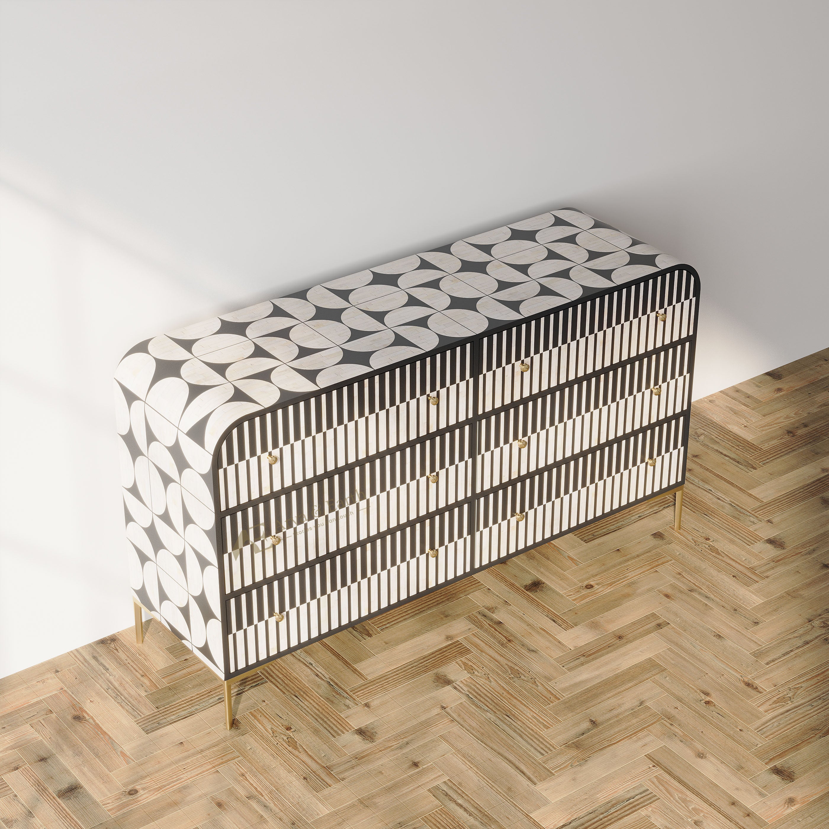 A modern three-drawer sideboard with a black and white geometric leaf pattern and gold legs, set against a white wall on a light wood herringbone floor.