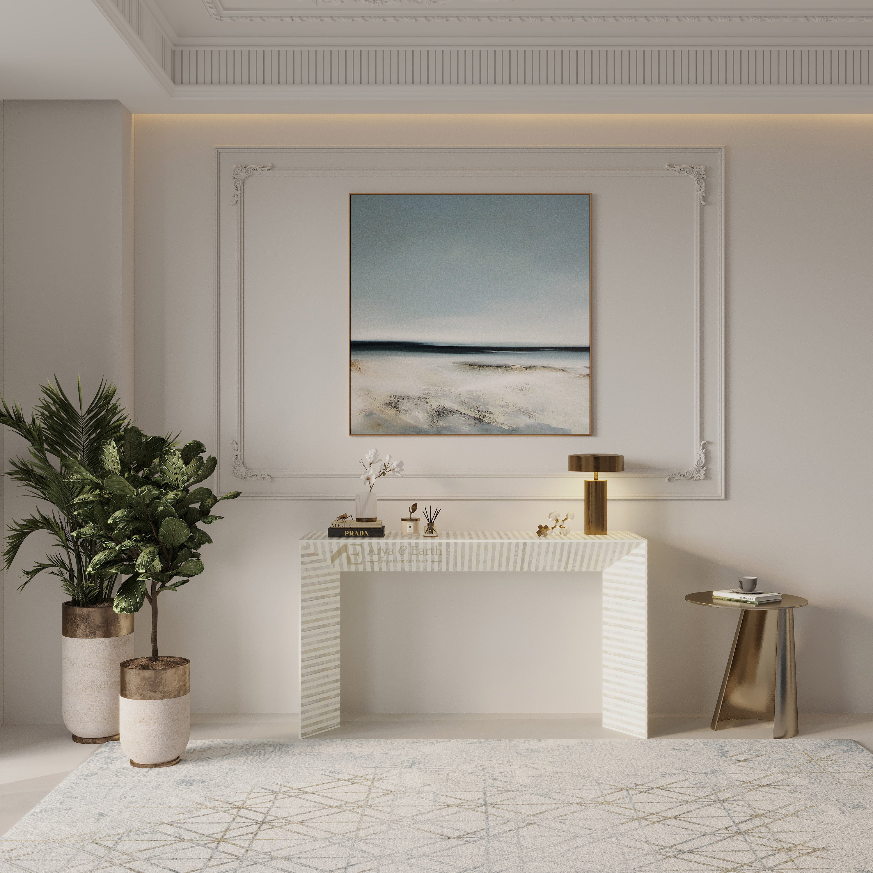 A framed abstract landscape painting with soft blue, gray, and beige tones hangs on a white wall above a white console table in a modern, elegant room with a potted plant and a small side table.