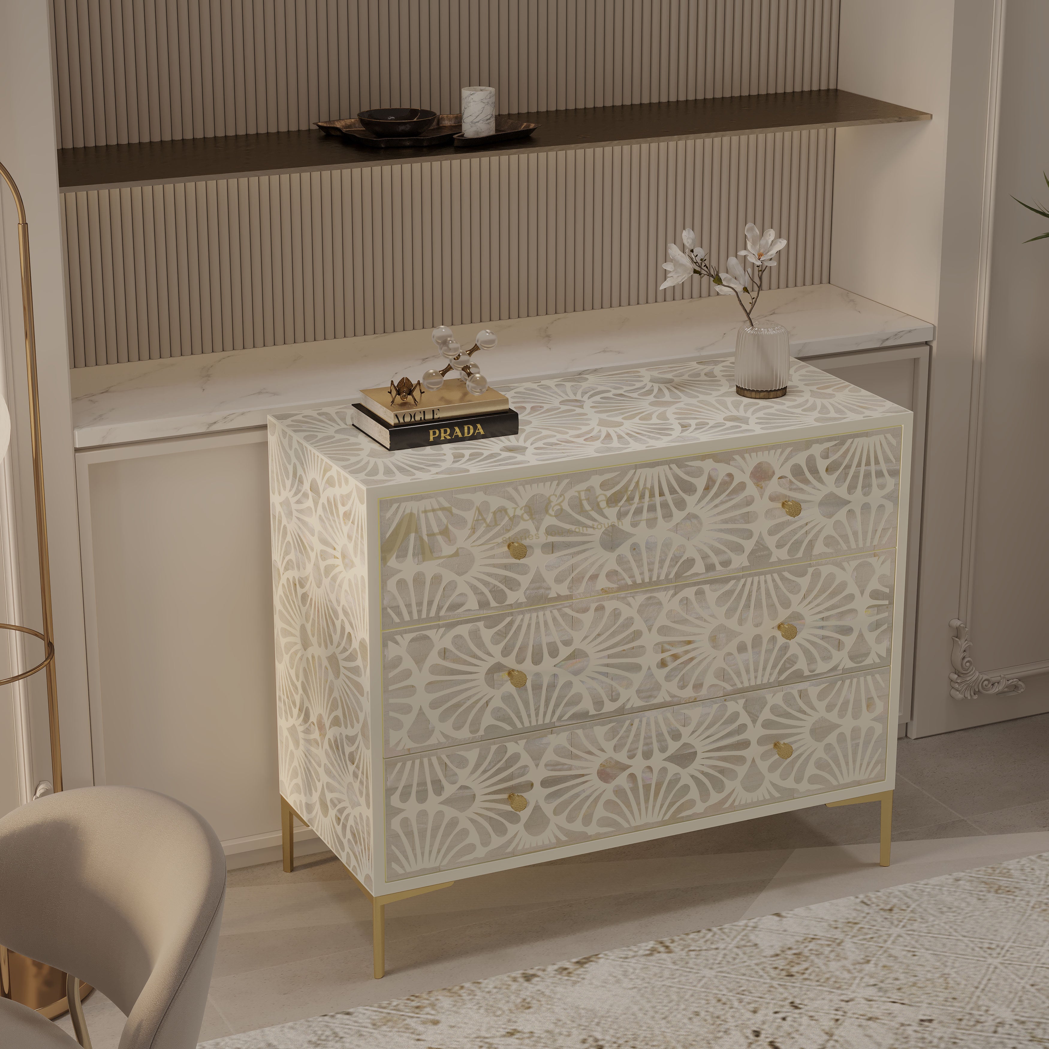 A three-drawer chest of drawers with an intricate white floral inlay pattern and gold legs, styled in a modern, warm-toned interior next to a marble-topped console table.