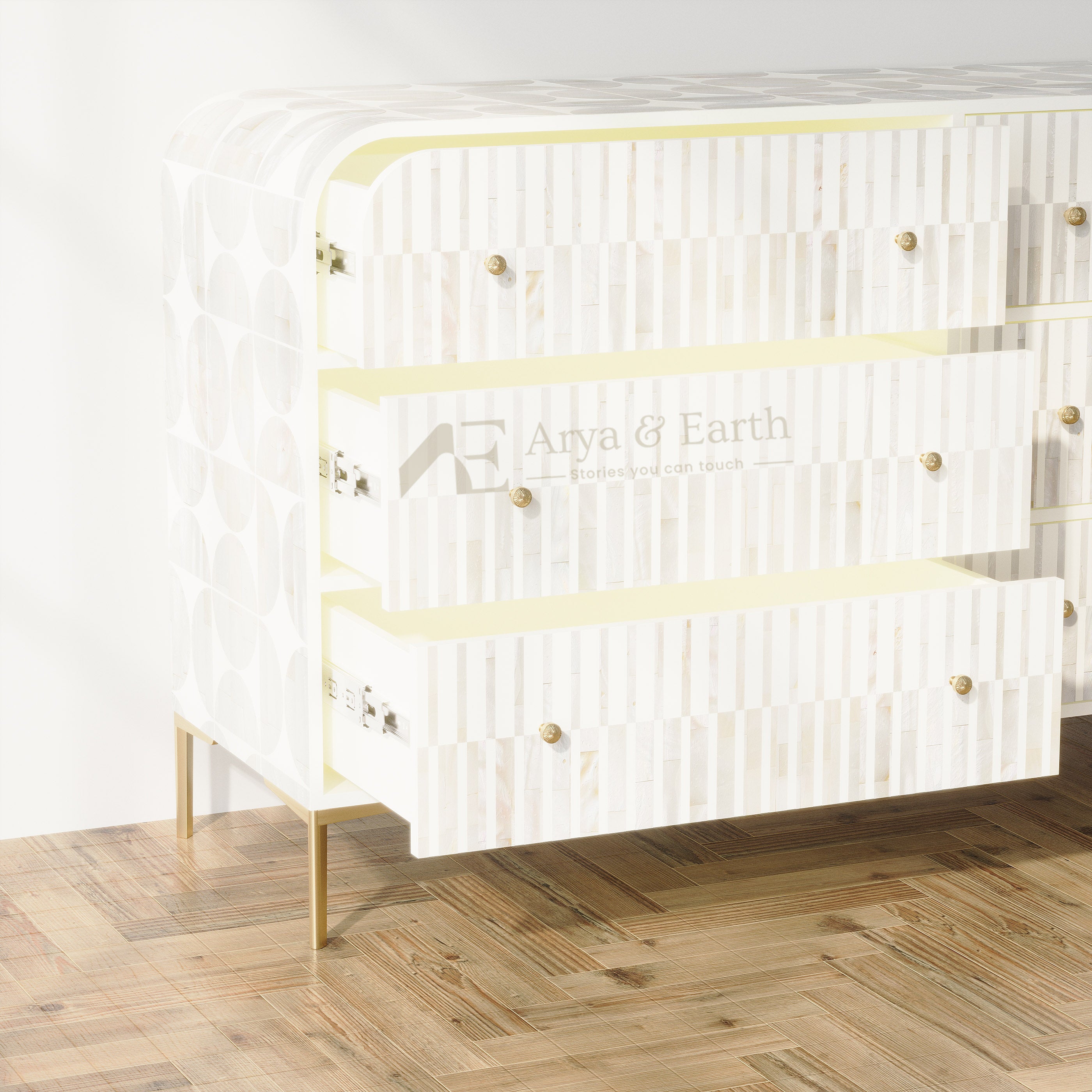 A white three-drawer chest of drawers with vertical wood slat detailing, brass knobs, and gold legs, shown on a wooden parquet floor against a white wall.