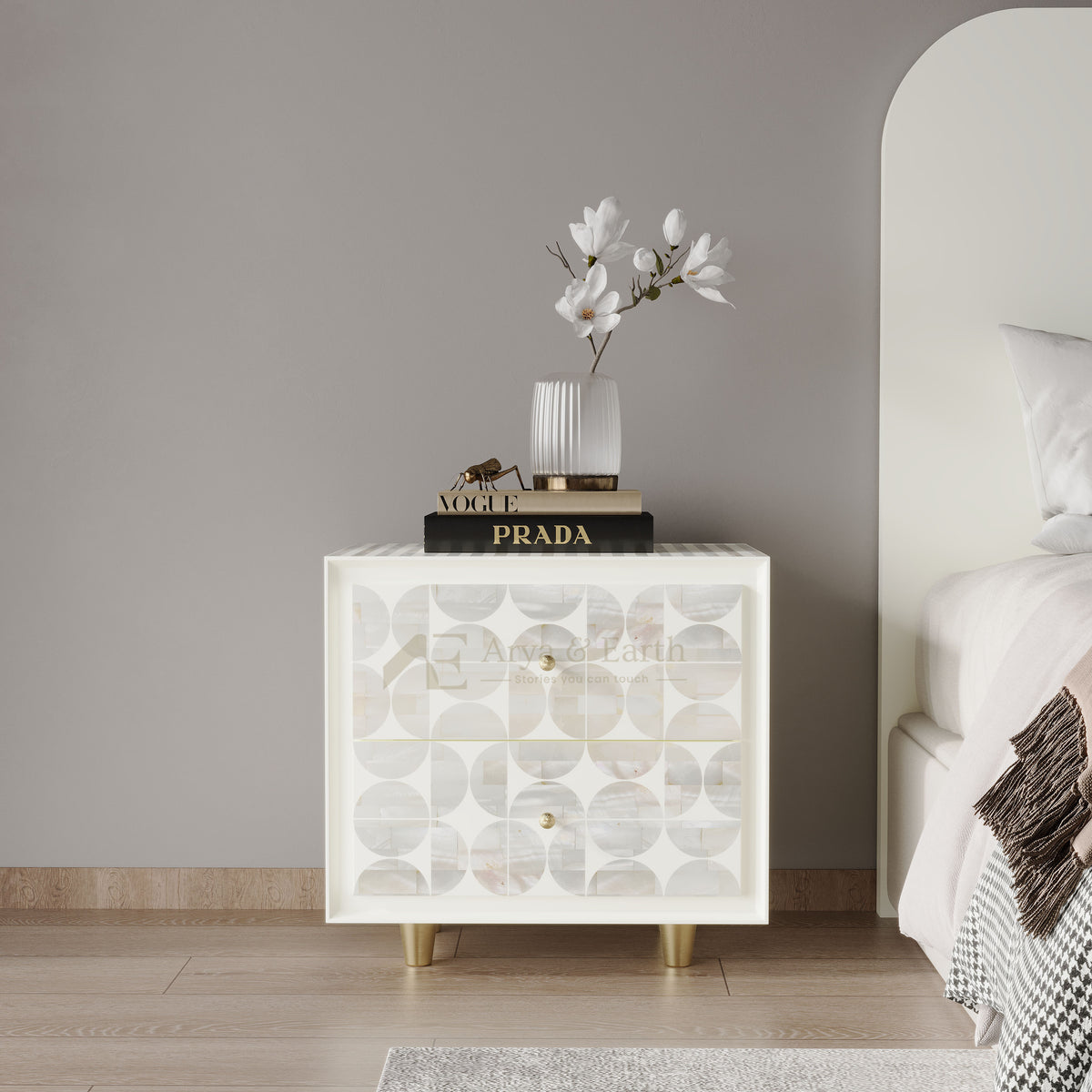 A modern two-drawer nightstand with a white frame and mother-of-pearl shell doors featuring a circular pattern, styled with a vase of white flowers and a book in a bedroom setting.