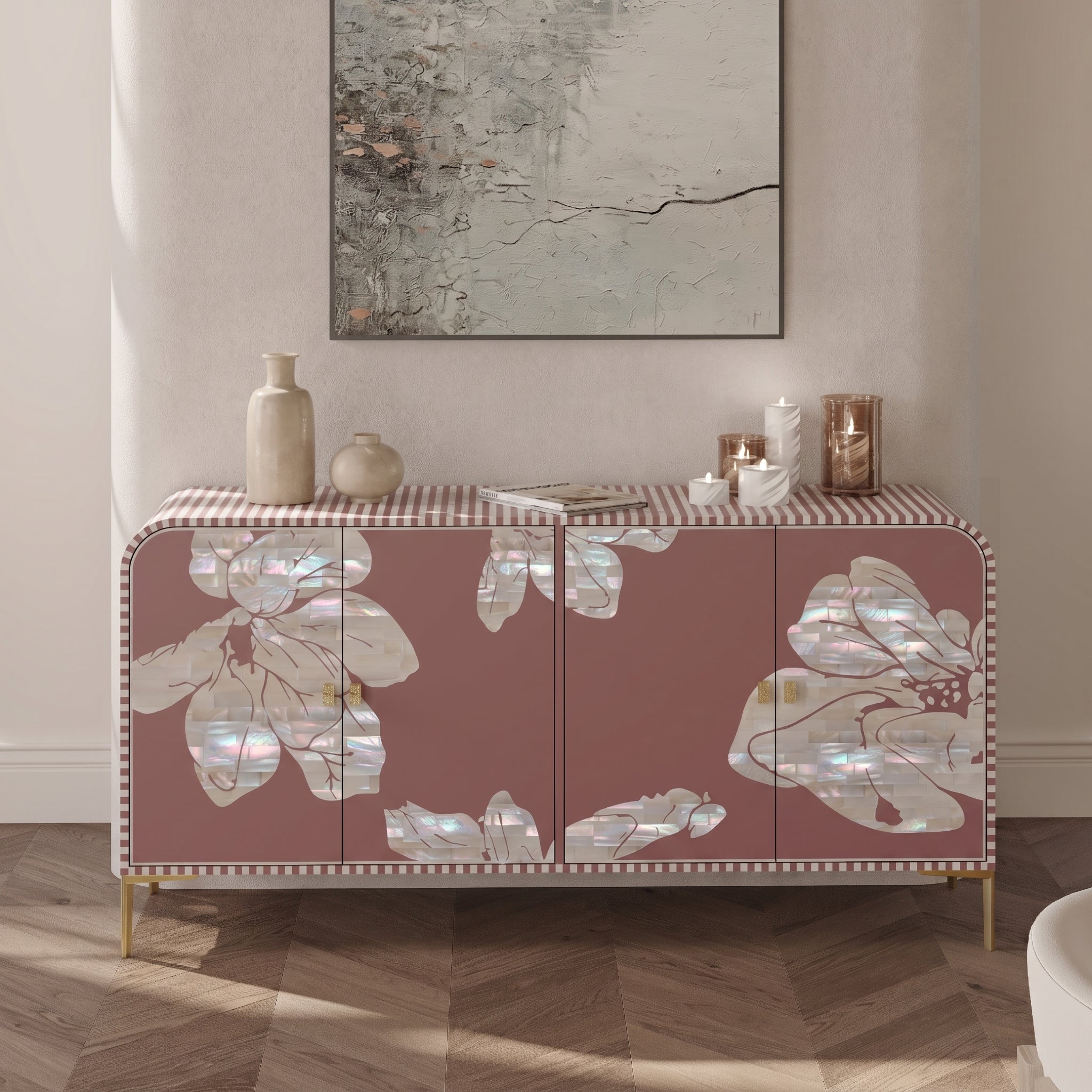 A pink sideboard cabinet with large iridescent floral inlays and a striped top, styled in a living room setting with decorative vases, candles, and a framed abstract print on the wall.