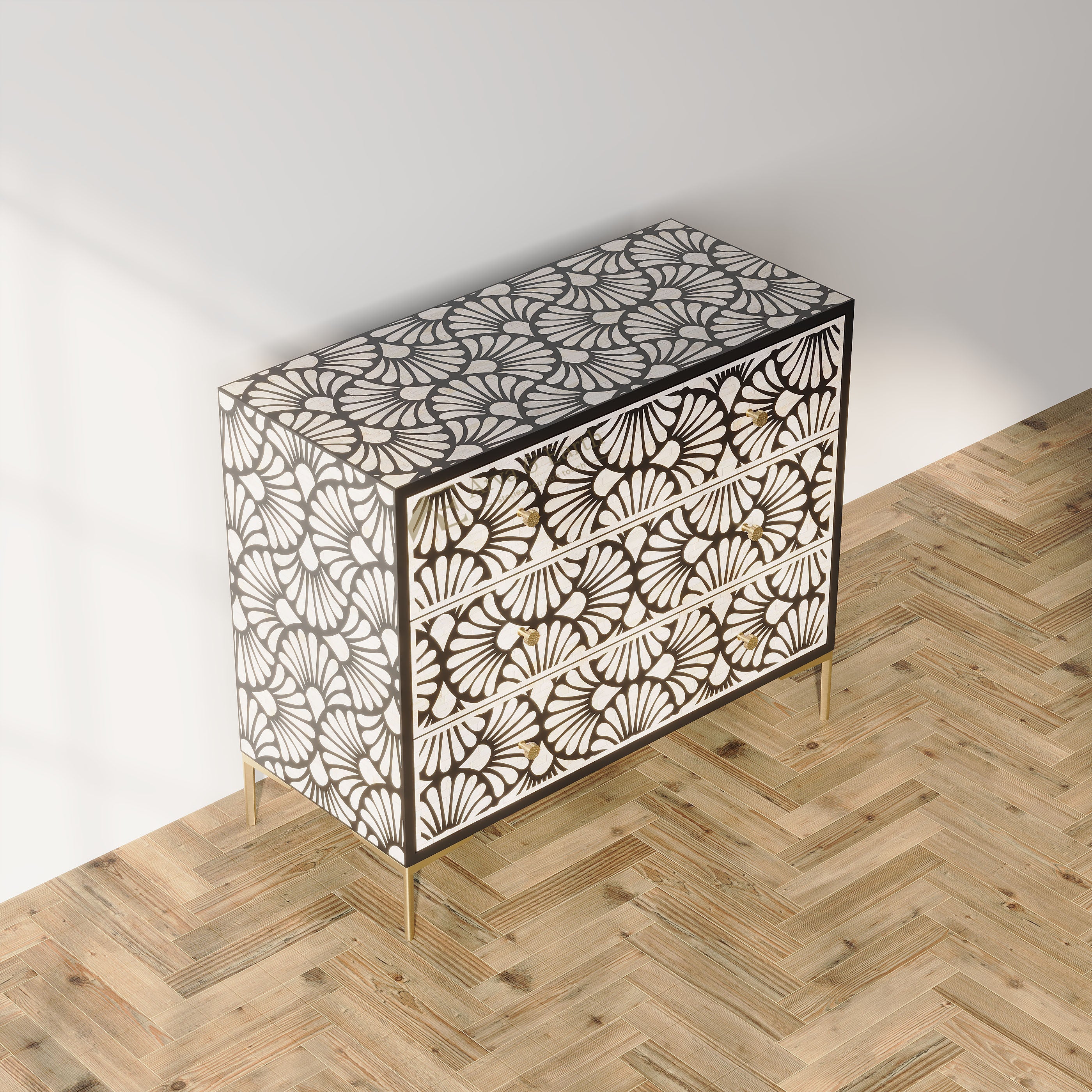A three-drawer chest with an intricate black and white fan-like geometric pattern and slim gold legs, set against a minimalist white wall and light wood herringbone floor.