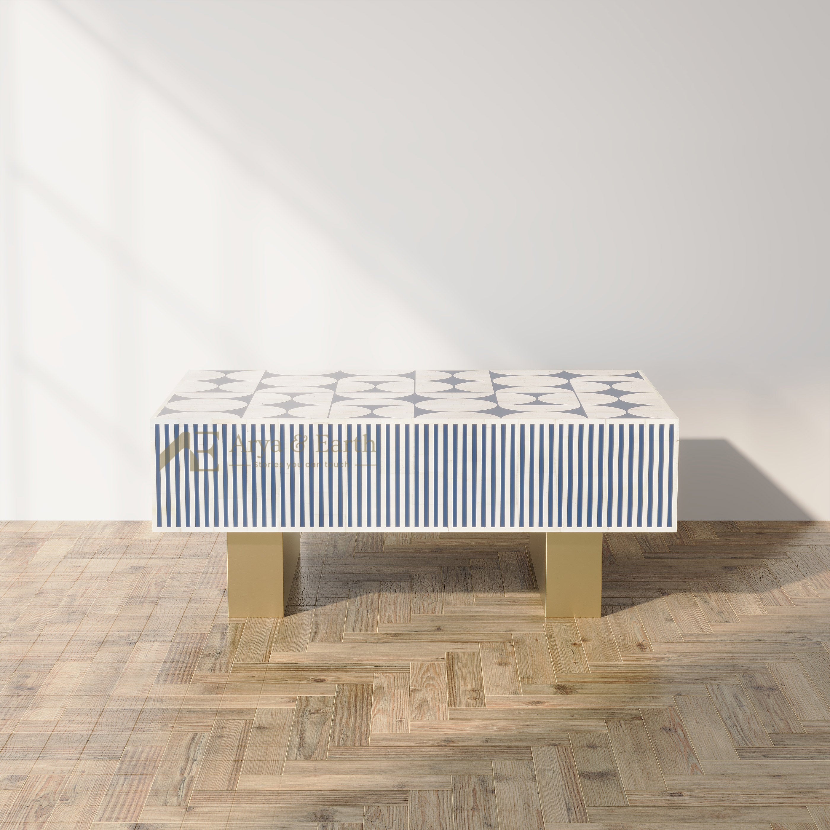 A modern rectangular console table with a white top featuring blue geometric patterns and blue-and-white vertical stripes, supported by two gold block legs, set against a white wall on a light wood herringbone floor.