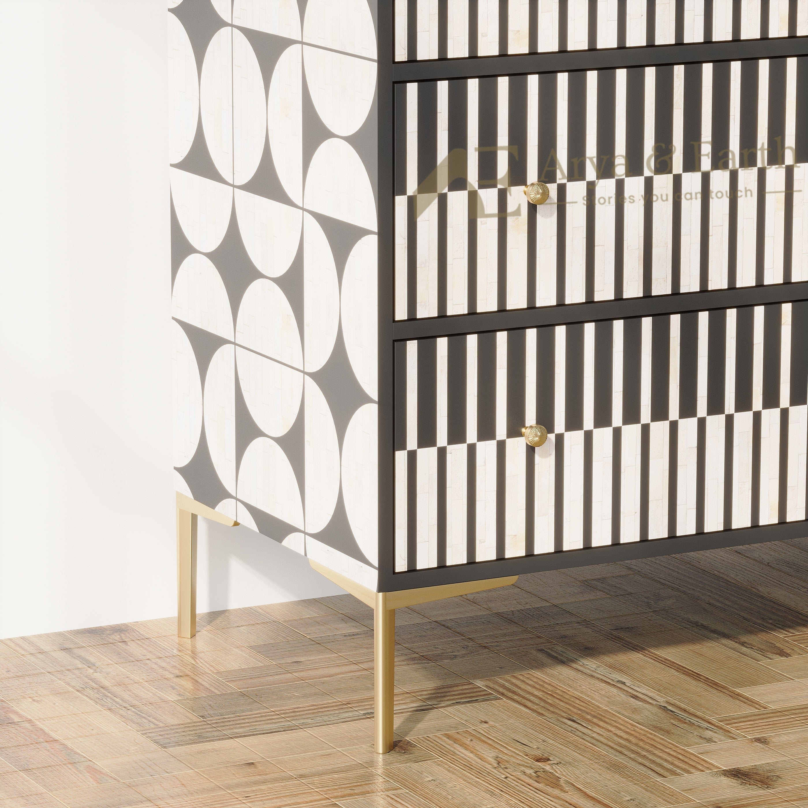 A modern three-drawer chest or cabinet with a black and white geometric striped pattern, featuring small gold knobs and slim gold metal legs, set against a white wall on a wooden parquet floor.