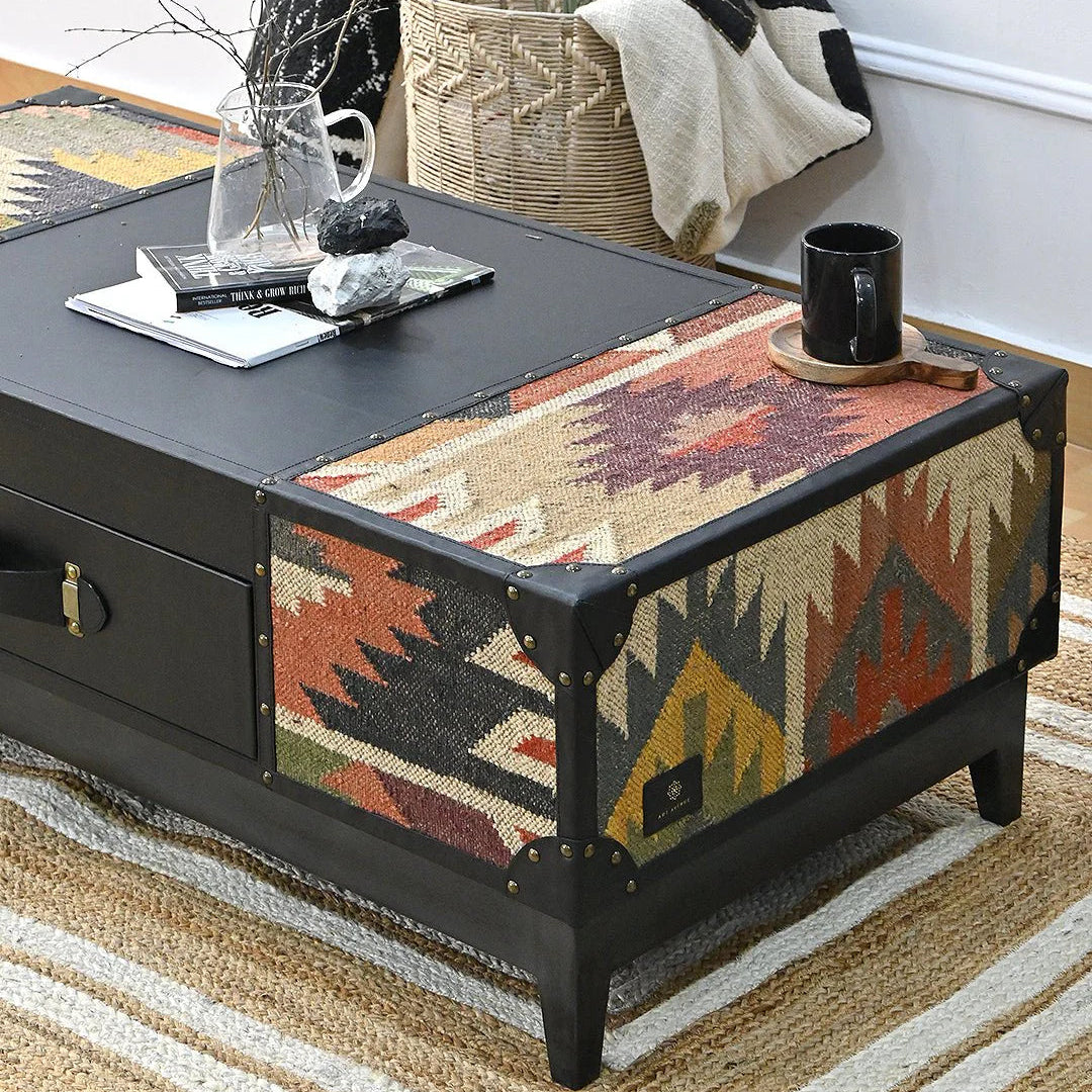 Coffee table with black finish and patterned fabric top in a living room setting.