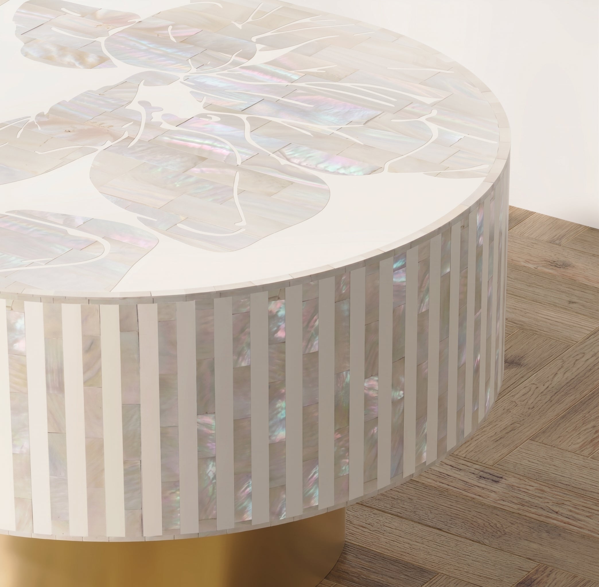 A round accent table featuring a white and iridescent mother-of-pearl inlay top with floral motifs and a fluted white side panel supported by a gold base, shown on a wood floor.