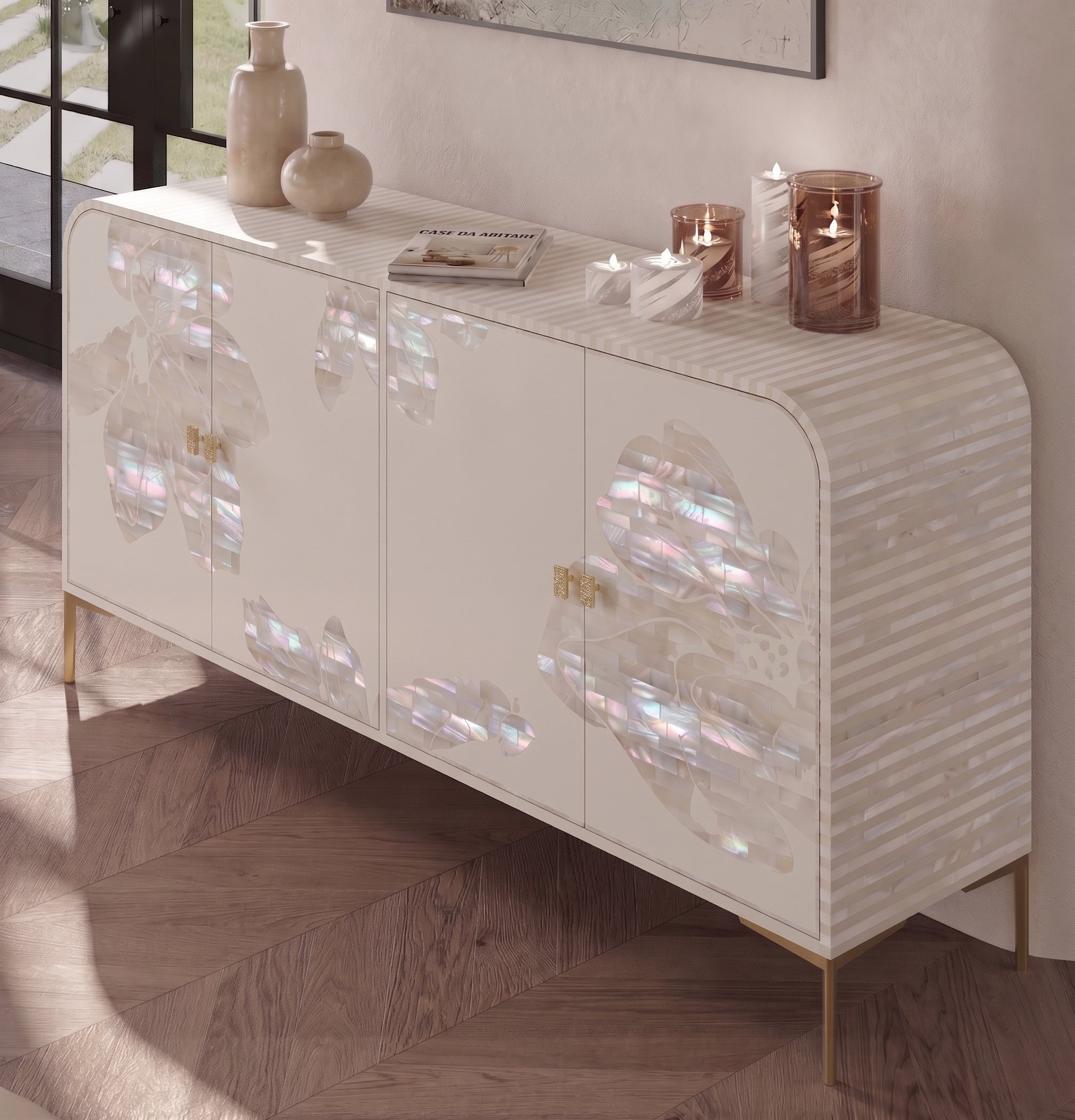 A modern sideboard cabinet with a glossy white finish, featuring iridescent mother-of-pearl floral inlays on the doors, striped side panels, and slim gold legs. The cabinet is styled in a room setting with decorative vases, candles, and a book on top, set against a neutral wall and herringbone wood flooring.