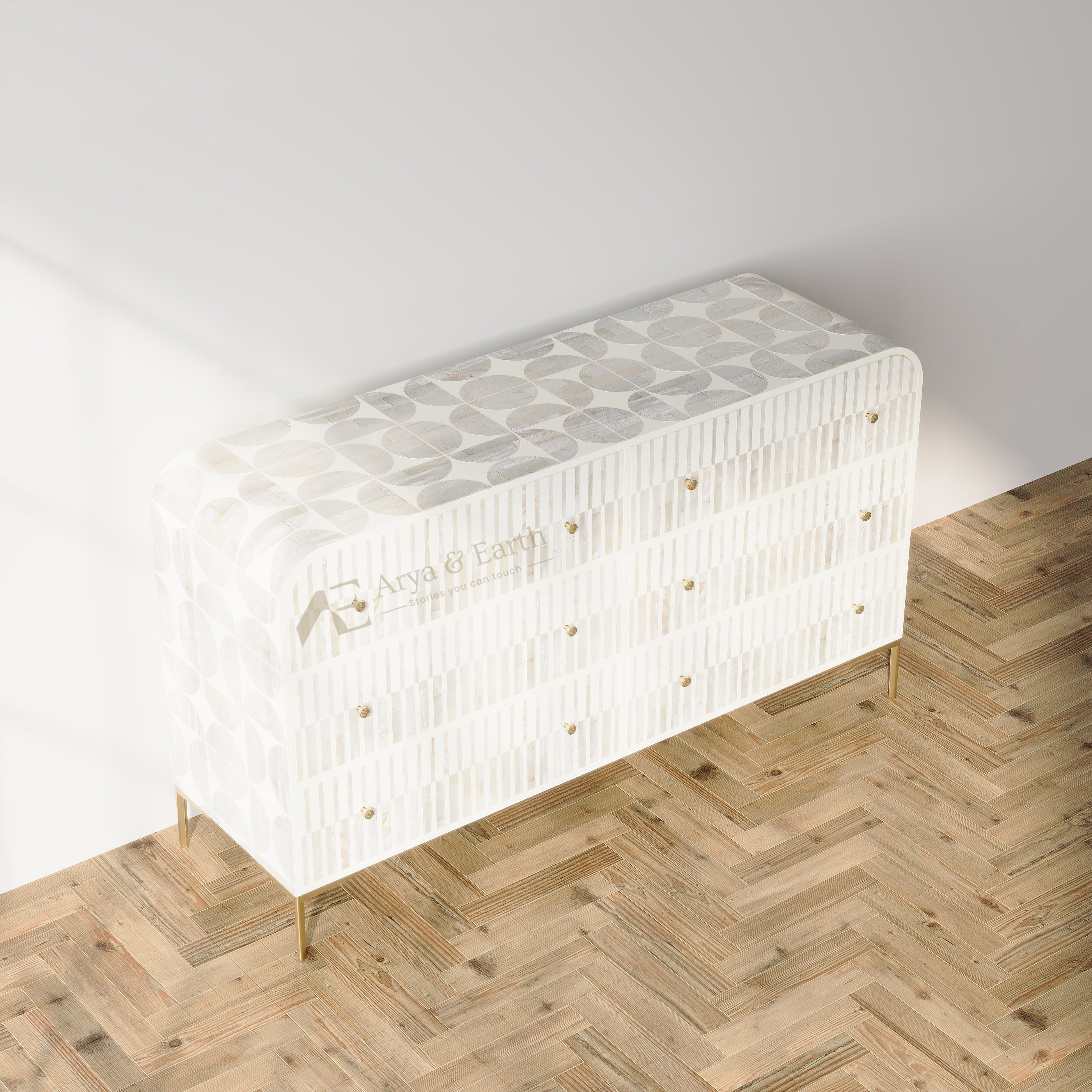A modern white sideboard or credenza with a textured geometric pattern on the top and drawers, supported by slim gold legs, set against a white wall on a light wood herringbone floor.