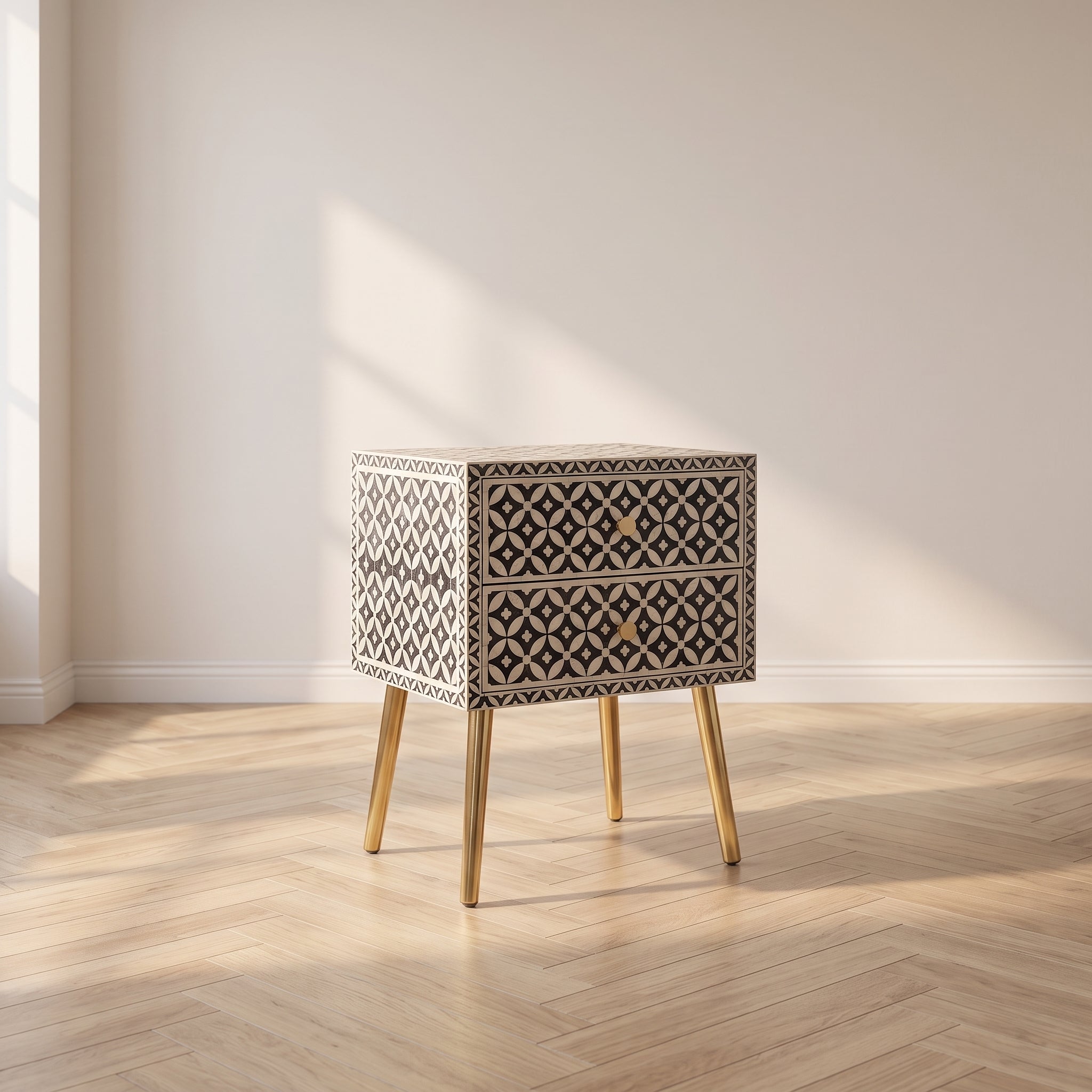 A two-drawer nightstand with a black and white geometric bone-inlay pattern and light wood legs, set in a minimalist room with a light wood herringbone floor and beige walls.