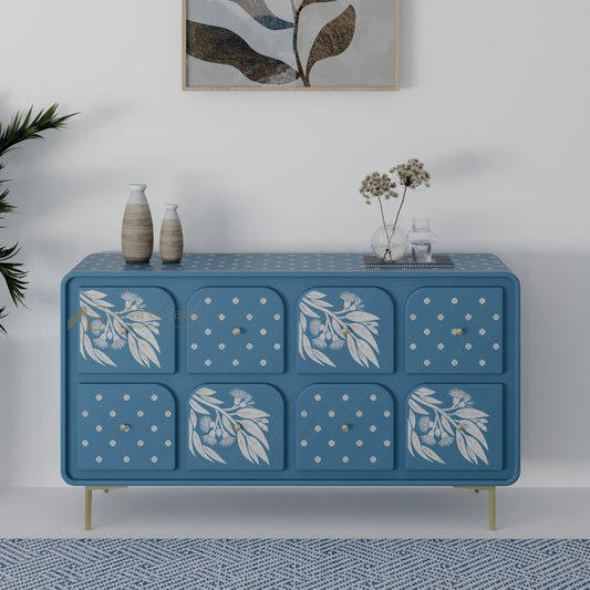 Blue chest of drawers with floral patterns on a white wall with a plant and abstract art.