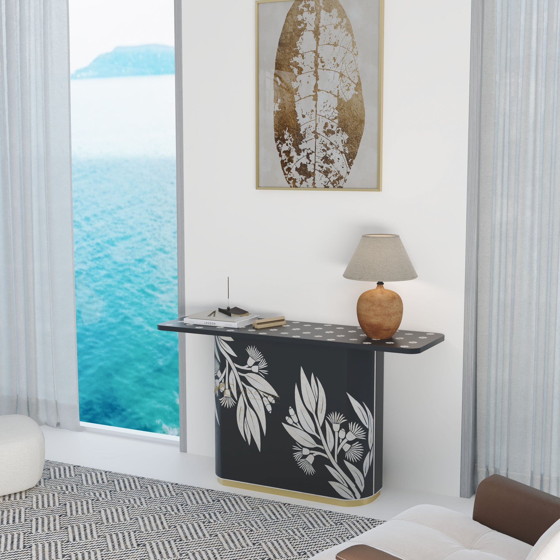 Modern interior with a black console table featuring white leaf patterns, a lamp, and a framed artwork by a large window with ocean view.