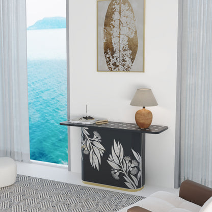 Modern interior with a black console table featuring white leaf patterns, a lamp, and a framed artwork by a large window with ocean view.